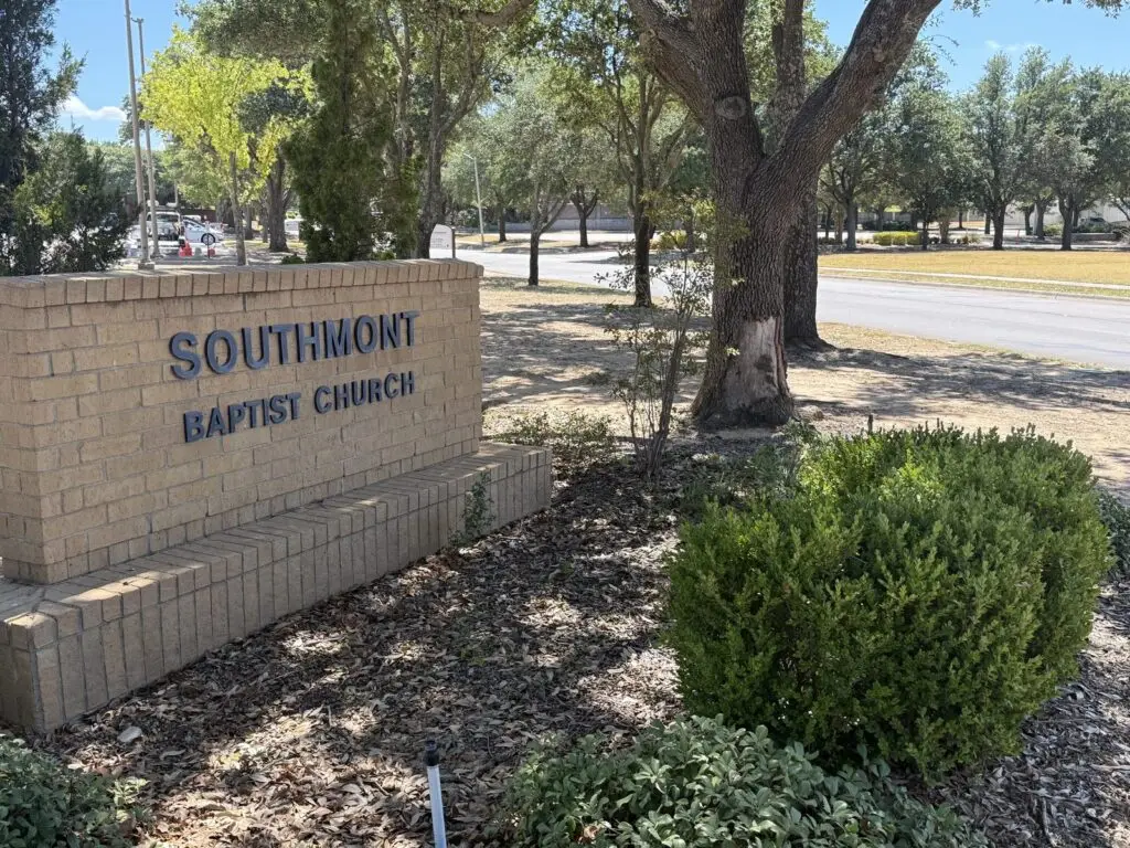 The brick entrance sign reading Southmont Baptist Church, beside a mulched bed with a few shrubs and a large live oak, with Pennsylvania Drive beyond.